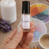 Hand holding a lavender essential oil roll-on with a diffuser, mug, and color wheel in the background.