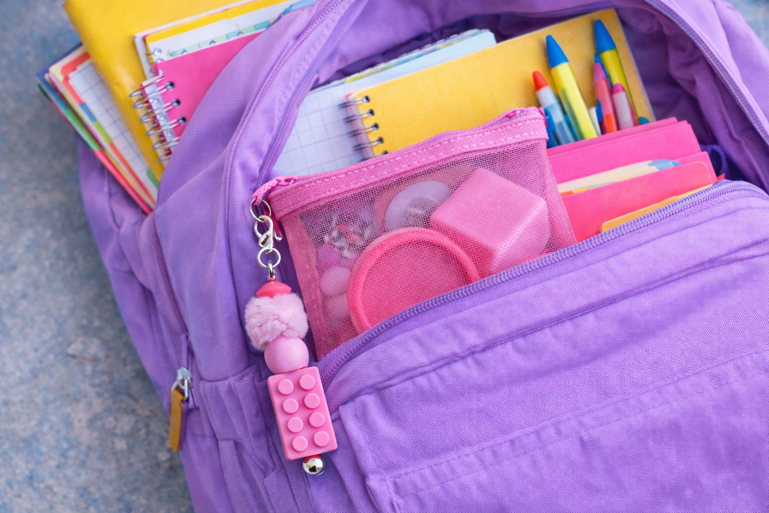 Purple backpack open to reveal Coping Skills Kids Kit stationery items including notebooks, pens, and a pink Lego-themed keychain.
