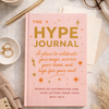 The Hype Journal pink hardcover guided journal by Coping Life displayed with coffee and glasses on neutral linen background