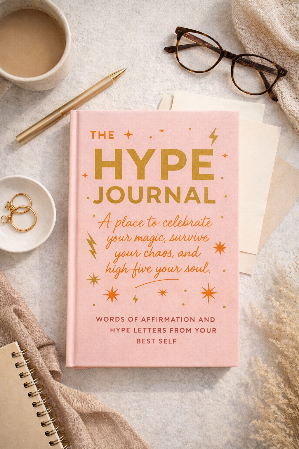 The Hype Journal pink hardcover guided journal by Coping Life displayed with coffee and glasses on neutral linen background